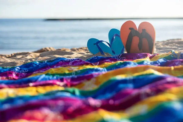 Güneşli bir kumsalın kumlarında terlikler ve renkli elbiseler.