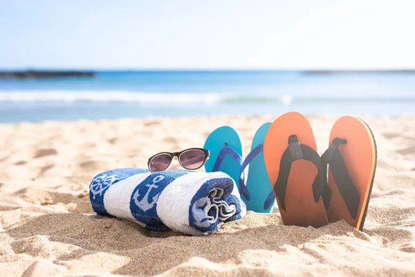 Plaj ayakkabıları, havlu ve kumsalda güneş gözlüğü.
