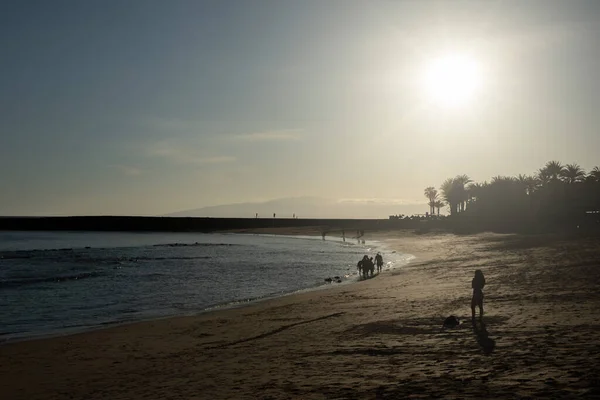 Güneşli bir sahilde gün batımında, arka planda insanlar var.