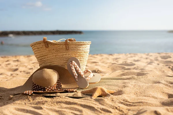 El çantası, parmak arası terlik ve güneşli bir kumsalın kumlarında şapka.