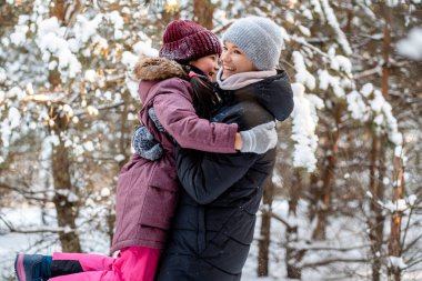 Ailece ormanda kış yürüyüşü. Çocuk büyütmek, aile alışkanlıkları. Anne ve kızı kışın güneşli ve dondurucu havada ormanda eğleniyorlar. Bir annenin kucaklaması..