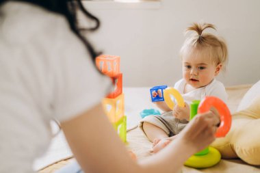 Anne ve çocuk arasındaki iletişim. Anne evde bebeğiyle oynuyor. Çocuk oyuncak piramidi topluyor. Doğumdan sonra bir kadının uyum içinde yaşaması.
