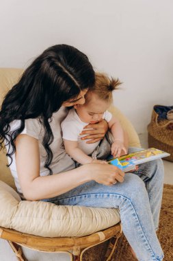 Erken çocukluk gelişimi. Anne ve çocuk arasındaki iletişim. Aile içinde sevgi ve nezaket. Annem bir sandalyede otururken bebeğine kitap okuyor..