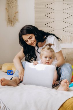 Evde çalışan serbest çalışan bir kadın. Çocuk annesinin internette dizüstü bilgisayarda çalışmasını engelliyor. Uzaktan kumanda. İnternette çalışıyorum. Bebek, annenin evde çalışmasına izin vermiyor..