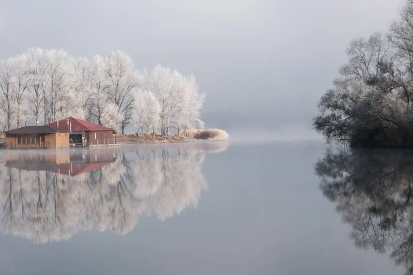 Huis aan het meer. De overgang van de natuur van herfst naar winter. mistige en zonnige ochtend op het meer. — Stockfoto