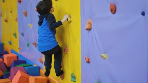Un niño en edad escolar trepa la pared de un muro de escalada. — Vídeos de Stock