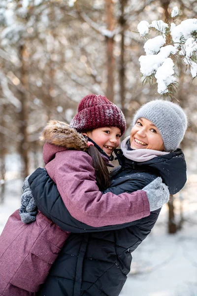 Paseo familiar de invierno en el bosque. Criar a un niño, hábitos familiares. Madre e hija se están divirtiendo en invierno en el bosque en un clima soleado y helado. Un abrazo de madres. — Foto de Stock