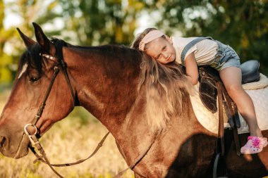 Uzun saçlı küçük sarışın bir kız sonbaharda günbatımında parkta ata biner ve ona sarılır. Sonbahar ata binme. Bir kızla bir atın arkadaşlığı..