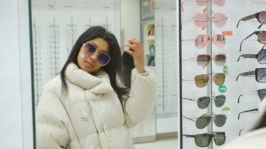 Koyu tenli genç bir kadın bir optik mağazasından moda gözlüklerini seçiyor. Afro-Amerikalı bir kadın dükkandan gözlük seçiyor..