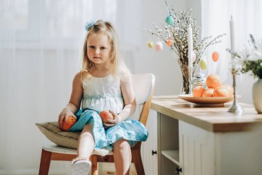 Paskalya tatili için hazırlık. Küçük bir kız, tatilin beklentisiyle elinde meyvelerle bir odada bir sandalyede oturuyor..