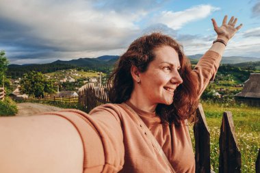 Dağlara yaz gezisi. Genç bir kadın gün batımında bir dağın tepesinde selfie çekiyor. Aktif yaşam tarzı, yürüyüş.