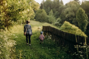 Çocuklu bir annenin aktif yaşam tarzı. Yazın dışarı çık. Çocuklarla dağlara yaz gezisi. Yazın bir dağ köyünde çocuğuyla bir annenin akşam yürüyüşü..