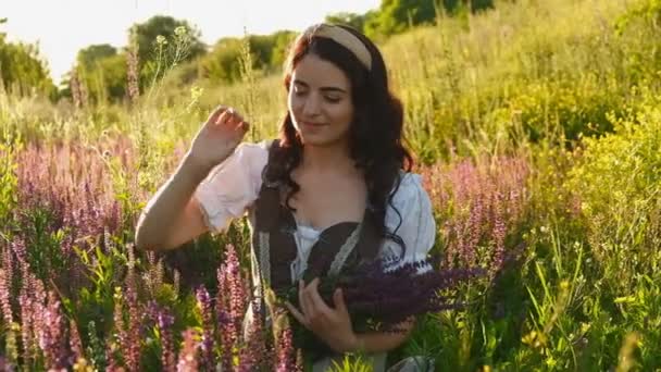 Młoda Kobieta Sukience Stoi Łące Fioletowymi Kwiatami Rękach Zachodzie Słońca — Wideo stockowe