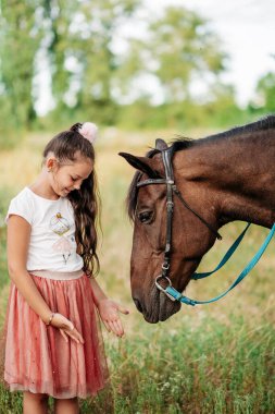 Çocuğun at ile olan etkileşimi. Çocuğun psikolojik rehabilitasyonu. Kız atı elleriyle besliyor..
