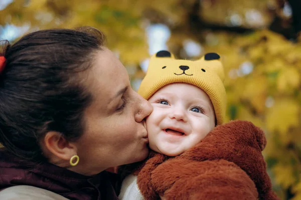 A woman walks in the park in autumn with her child. A young woman holds her baby in her arms and stands under a tree. Family walks in autumn in the park.