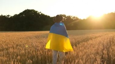 A man stands in a wheat field at sunset and holds the flag of Ukraine in his hands. Ukraine's victory over Russia in the war. Veteran's Day of the Russian-Ukrainian War. Ukraine won.