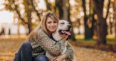 A young blonde woman is playing in the autumn park with her labrador. Evening walk with a labrador. Love for pets.