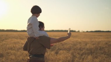 A young beautiful brunette plays with her little child on a walk in a wheat field. Wheat shortage in the world. Family walk outside the city in summer at sunset.
