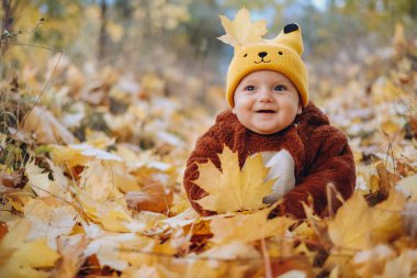 The kid sits in yellow leaves in the park for a walk. Family autumn walk in the evening in the park with children. Happy motherhood.