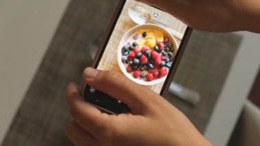 A man takes a picture of a bowl of fresh and appetizing food on the table. Filming food with a smartphone. A vlogger creates content for his channel.