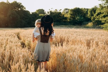 A young beautiful brunette plays with her little child on a walk in a field of sunflowers. Deficit of sunflower oil in the world. Family walk in the countryside in summer on