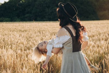 A young beautiful brunette plays with her little child on a walk in a field of sunflowers. Deficit of sunflower oil in the world. Family walk in the countryside in summer on