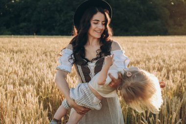 A young beautiful brunette plays with her little child on a walk in a field of sunflowers. Deficit of sunflower oil in the world. Family walk in the countryside in summer on