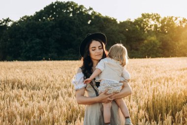 A young beautiful brunette plays with her little child on a walk in a field of sunflowers. Deficit of sunflower oil in the world. Family walk in the countryside in summer on