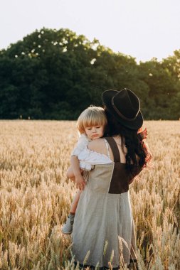 A young beautiful brunette plays with her little child on a walk in a field of sunflowers. Deficit of sunflower oil in the world. Family walk in the countryside in summer on