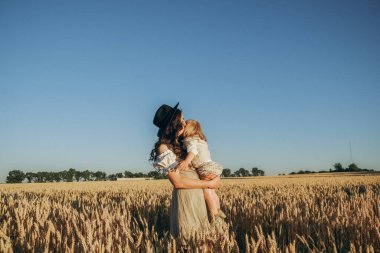 A young beautiful brunette plays with her little child on a walk in a field of sunflowers. Deficit of sunflower oil in the world. Family walk in the countryside in summer on