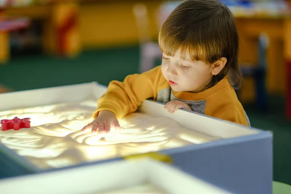 Creative child development. Baby draws sand on glass. Early development of children. Development of shallow motility and tactile sensations.