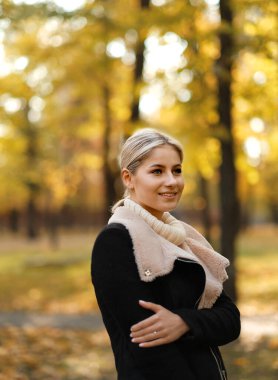 Genç güzel sarışın kadın sonbahar parkında yürüyor. Parkta sonbahar yürüyüşleri. Sonbaharda aktif tatiller.