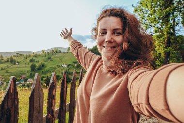 Dağlara yaz gezisi. Genç bir kadın gün batımında bir dağın tepesinde selfie çekiyor. Aktif yaşam tarzı, yürüyüş.