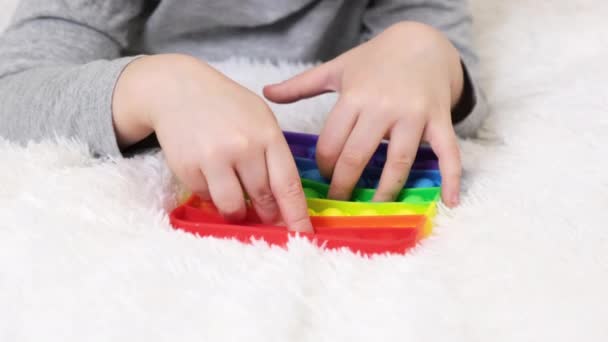 Kleine Jungenhände spielen ein lehrreiches Spiel. Bunte antistress-sensorische Spielzeug-Fidget-Push-Push in Kleinkindhänden. Antistress trendy pop it toy. Regenbogensensorik zappelt. Neues trendiges Silikonspielzeug — Stockvideo