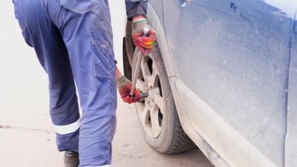 Hombre con esfuerzo fija o gira una rueda en un coche Volvo a mano, el proceso de quitar o fijar una rueda con una herramienta de mano en casa, un trabajo de hombre de reemplazar el caucho en un coche. Rusia, Moscú, 10.16.2021 — Vídeo de stock