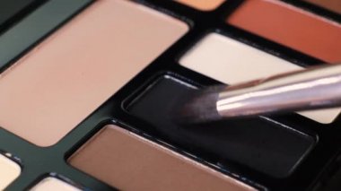 Fırça siyah pigmentleri makyaj malzemelerinde kullanmak üzere üst üste yığar. Göz farı paletiyle çalışan sanatçı, farklı toz renkleri. Çalışma sürecinin ayrıntıları, güzellik endüstrisindeki aletler. Dekoratif kozmetik.