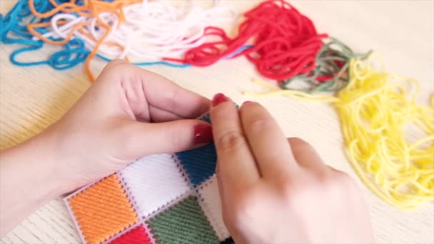 Las manos femeninas con uñas rojas bordan un patrón geométrico con hilos de lana. El concepto de bordado, costura, pasatiempos y ocio en casa. Movimiento lento — Vídeos de Stock