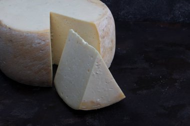 Eski çedar peyniri. Tekerlekli peynir. Koyu ahşap zeminde yıllanmış çedar peyniri çarkı.