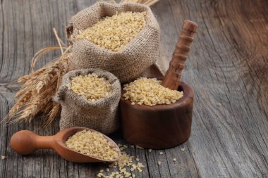 Ahşap zemin üzerinde kuru bulgur taneleri. Vejetaryen mutfağı. Yemek pişirmek için kuru bulgur. Buharda pişirilmiş, kurutulmuş ve ezilmiş buğday taneleri, Orta Doğu mutfağının bir parçası.