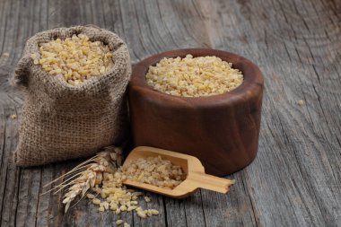 Ahşap zemin üzerinde kuru bulgur taneleri. Vejetaryen mutfağı. Yemek pişirmek için kuru bulgur. Buharda pişirilmiş, kurutulmuş ve ezilmiş buğday taneleri, Orta Doğu mutfağının bir parçası.