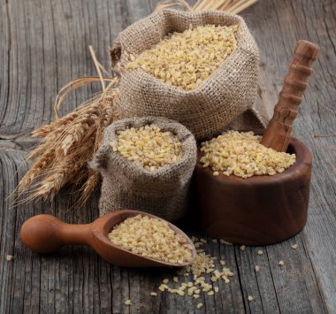 Ahşap zemin üzerinde kuru bulgur taneleri. Vejetaryen mutfağı. Yemek pişirmek için kuru bulgur. Buharda pişirilmiş, kurutulmuş ve ezilmiş buğday taneleri, Orta Doğu mutfağının bir parçası.