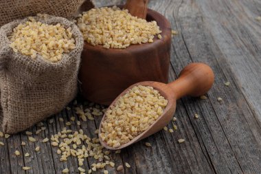 Ahşap zemin üzerinde kuru bulgur taneleri. Vejetaryen mutfağı. Yemek pişirmek için kuru bulgur. Buharda pişirilmiş, kurutulmuş ve ezilmiş buğday taneleri, Orta Doğu mutfağının bir parçası.