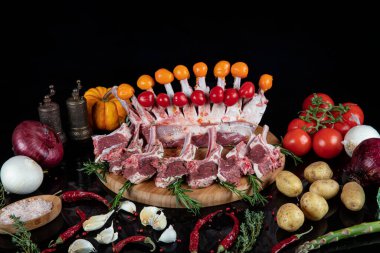 Çiğ taze kuzu pirzolası ve yeşil otlar. Kuzu pirzolası karanlık arka planda pişmeye hazır. Biberiye ve sebzeli çiğ pirzola..