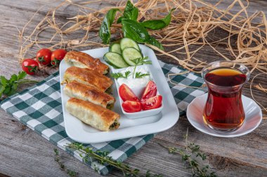 Beyaz tabakta ıspanaklı Türk çorbası. Geleneksel Türk hamur işi, rulo borek. Ispanak Borek, domates, salatalık ve çay..