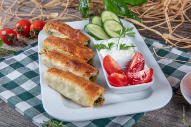 Beyaz tabakta ıspanaklı Türk çorbası. Geleneksel Türk hamur işi, rulo borek. Ispanak Borek, domates, salatalık ve çay..