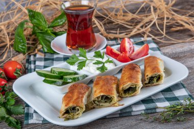 Beyaz tabakta ıspanaklı Türk çorbası. Geleneksel Türk hamur işi, rulo borek. Ispanak Borek, domates, salatalık ve çay..