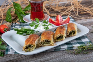 Beyaz tabakta ıspanaklı Türk çorbası. Geleneksel Türk hamur işi, rulo borek. Ispanak Borek, domates, salatalık ve çay..