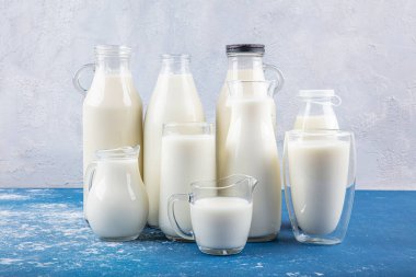 Temiz kavanozlardaki saf süt içecekleri ve şişeler mavi arka planda doğal olarak sağlıklı gıdalardır. Bir şişe süt ve bir bardak süt mavi arka plandaki ahşap bir masada.. 