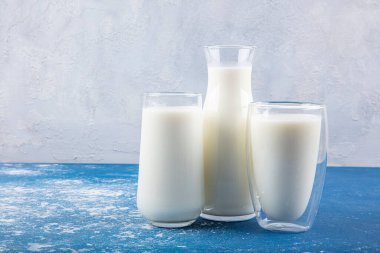Temiz kavanozlardaki saf süt içecekleri ve şişeler mavi arka planda doğal olarak sağlıklı gıdalardır. Bir şişe süt ve bir bardak süt mavi arka plandaki ahşap bir masada.. 