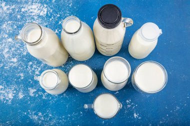 Temiz kavanozlardaki saf süt içecekleri ve şişeler mavi arka planda doğal olarak sağlıklı gıdalardır. Bir şişe süt ve bir bardak süt mavi arka plandaki ahşap bir masada.. 